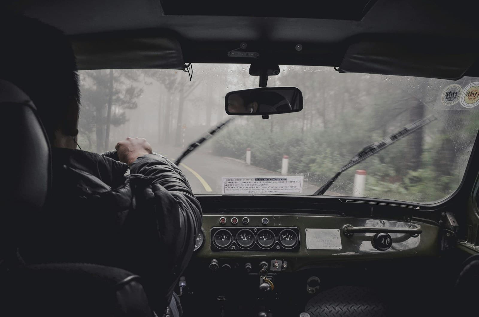 Driver in a dark jacket in rainy weather with the wipers running and rain on the windshield