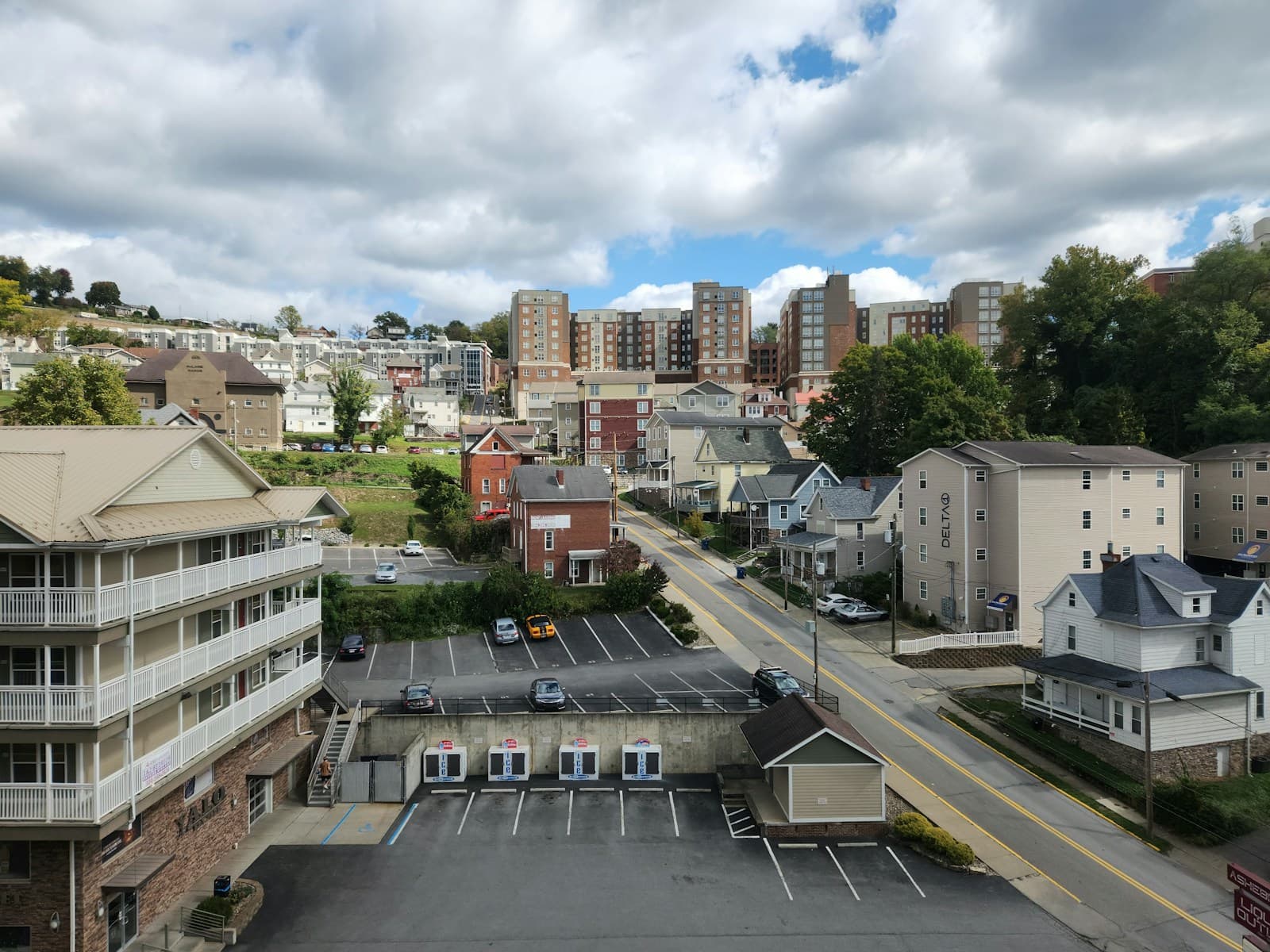 Aerial view of suburban town with apartment buildings, houses, parking lots and tree-lined streets under cloudy sky