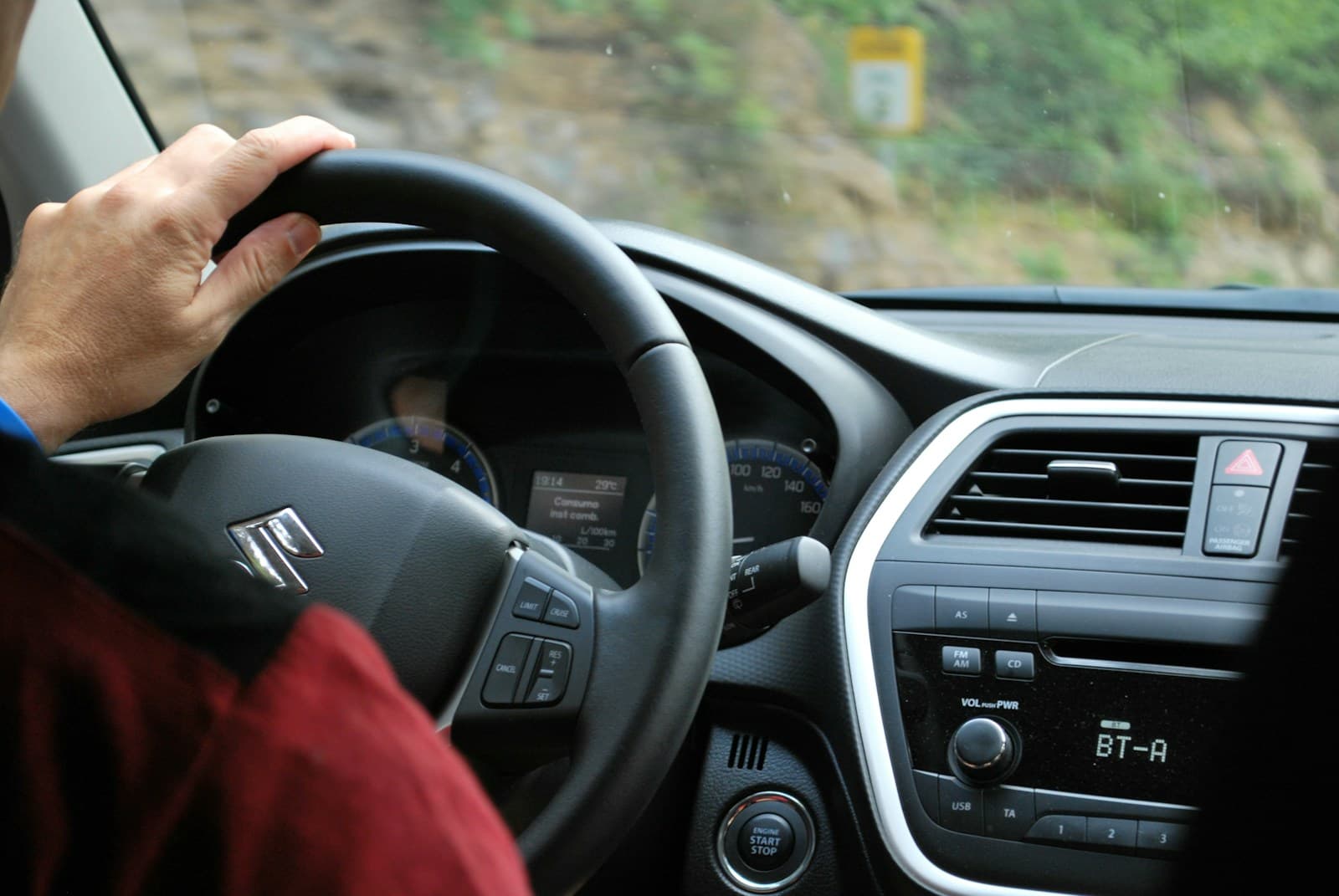Hand in a red sleeve on the Suzuki steering wheel of a car in motion