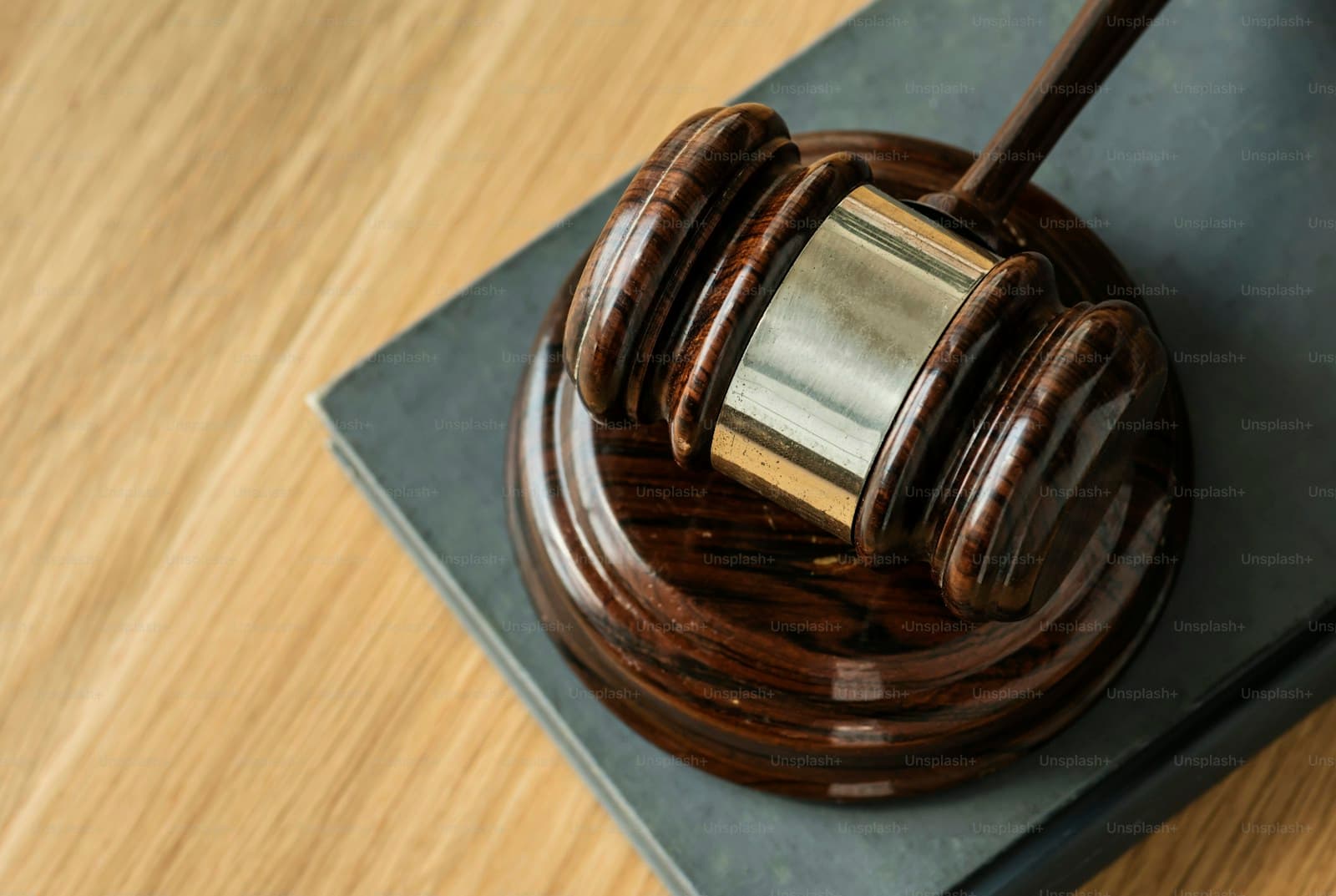 Wooden judge's gavel with metal band on dark base sitting on light wood surface