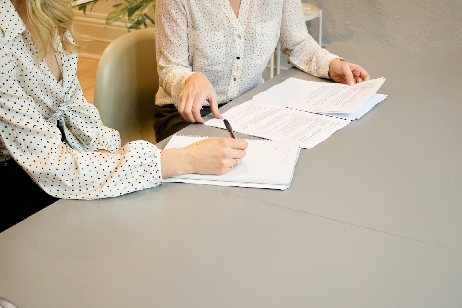 Two women at a white table, one signing documents as the other guides her