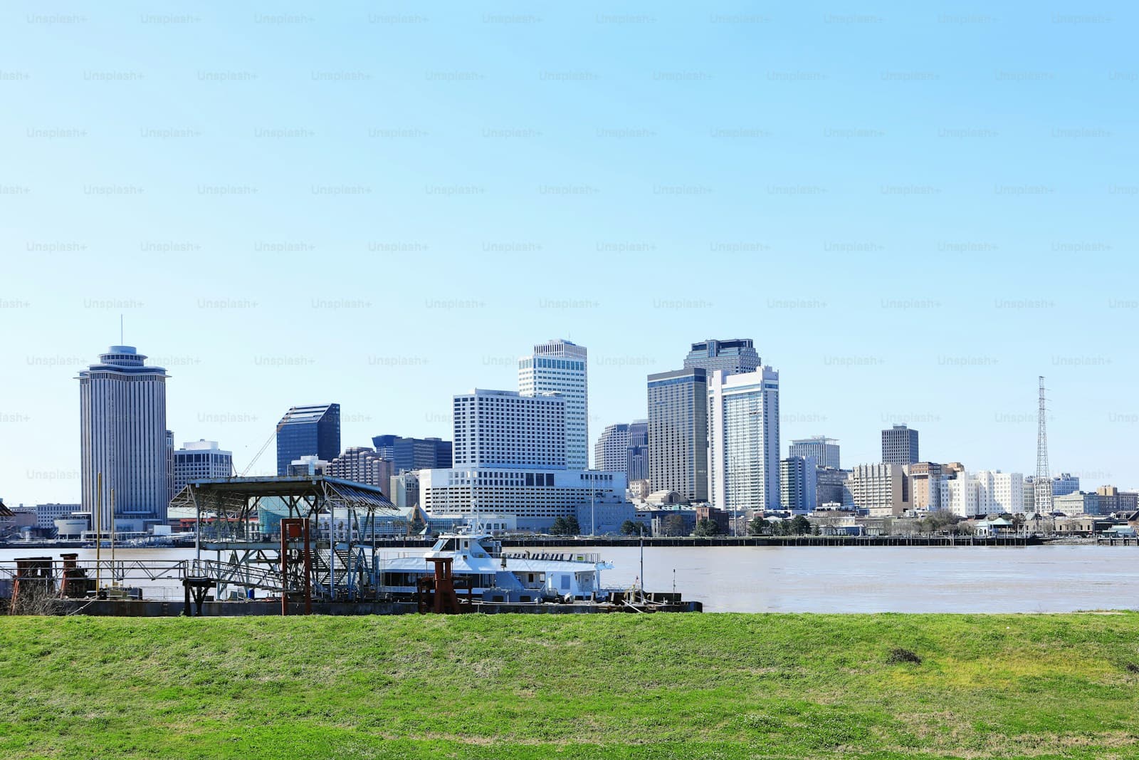 City skyline with tall buildings viewed across water with green grass in foreground on clear day