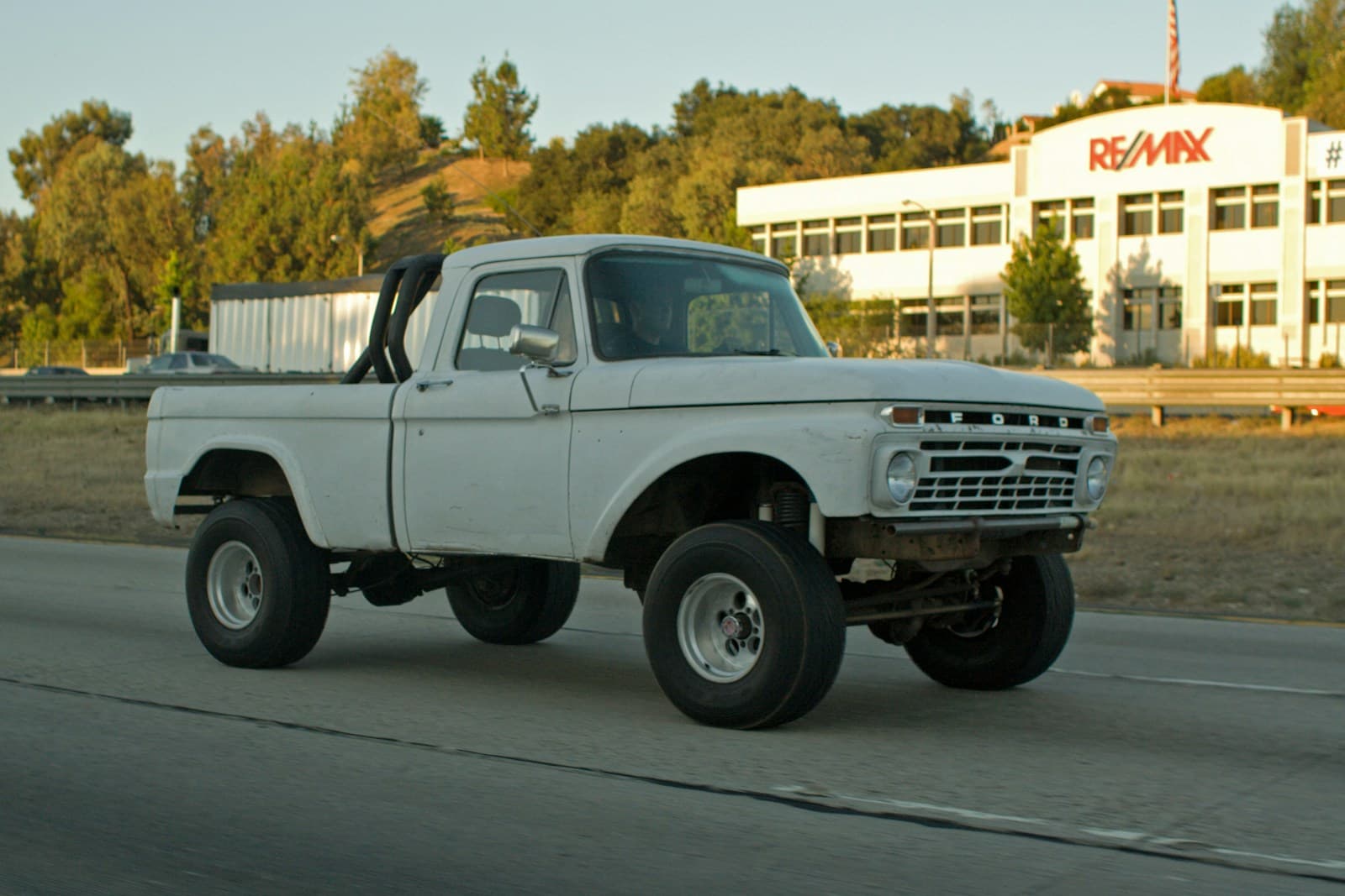 White vintage Ford pickup with oversized tires parked outside an office building