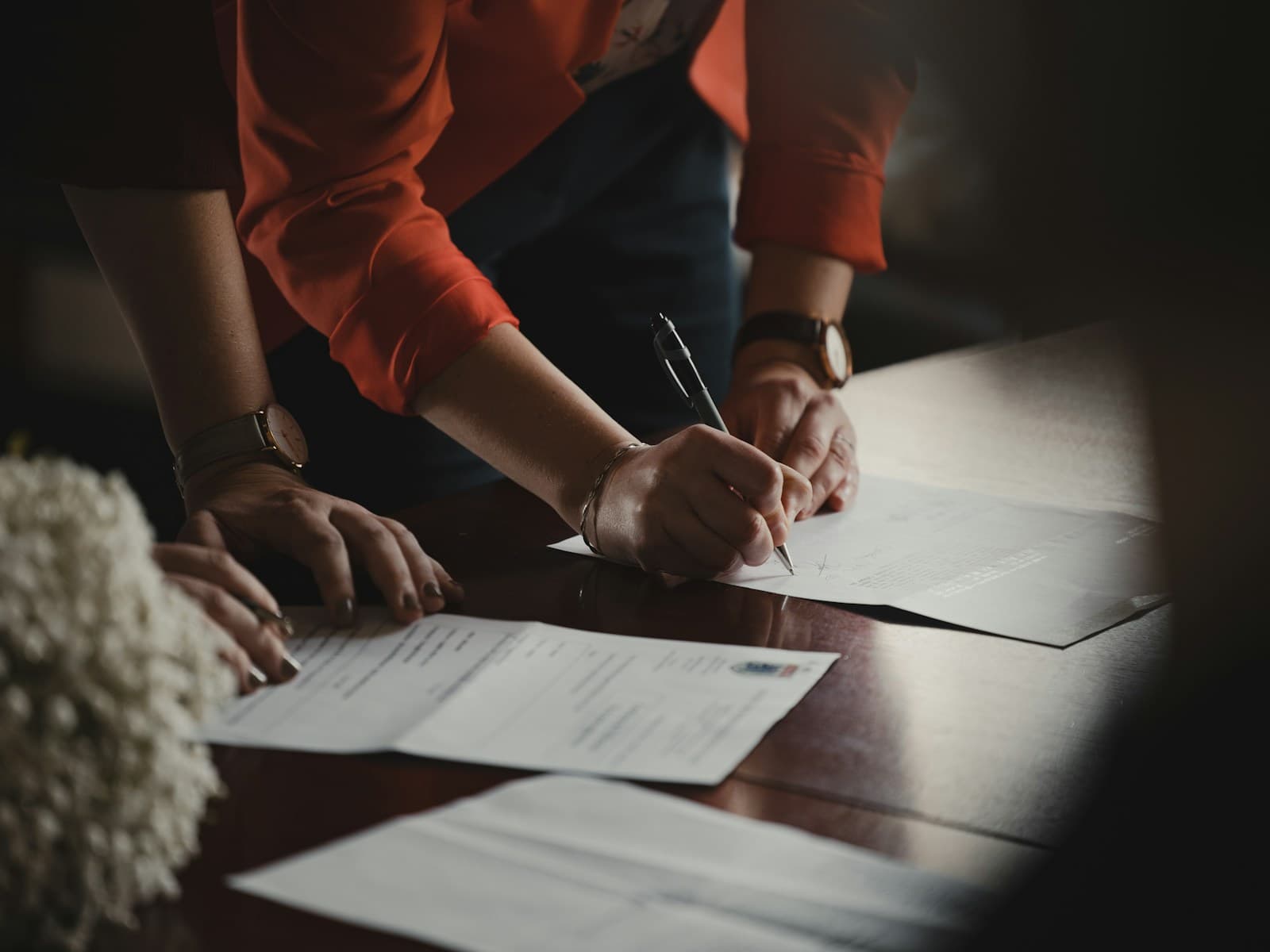 Two people signing documents at a wooden table, one holding a pen
