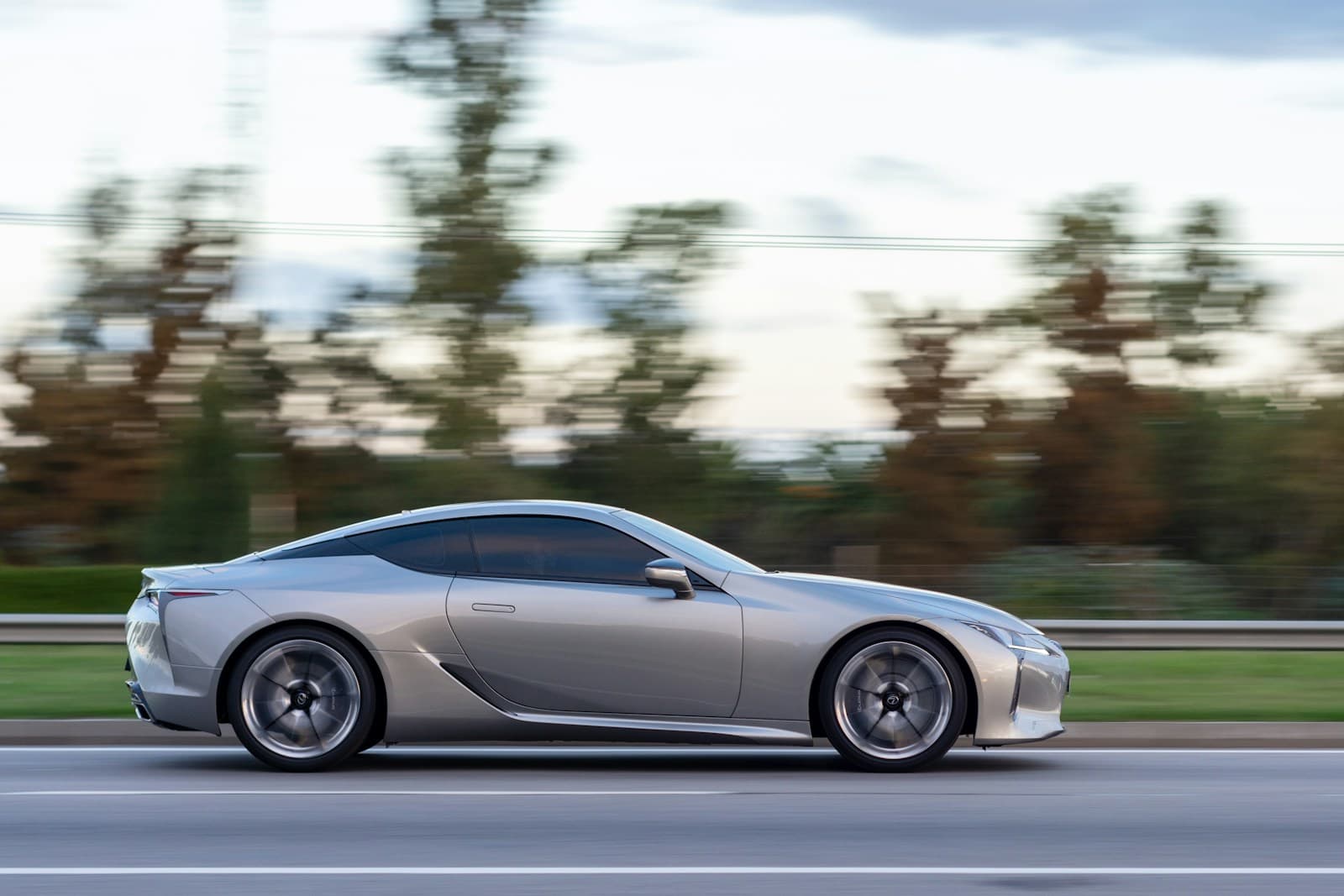 Silver luxury sports coupe driving on road with motion blur background