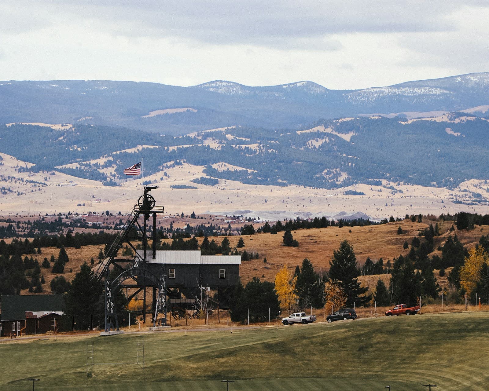 Historic mining headframe structure in golden autumn landscape with rolling hills and mountains in background