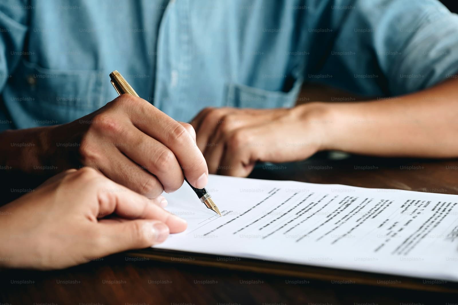 Person in a light blue shirt signing a multi-page document at a wooden table