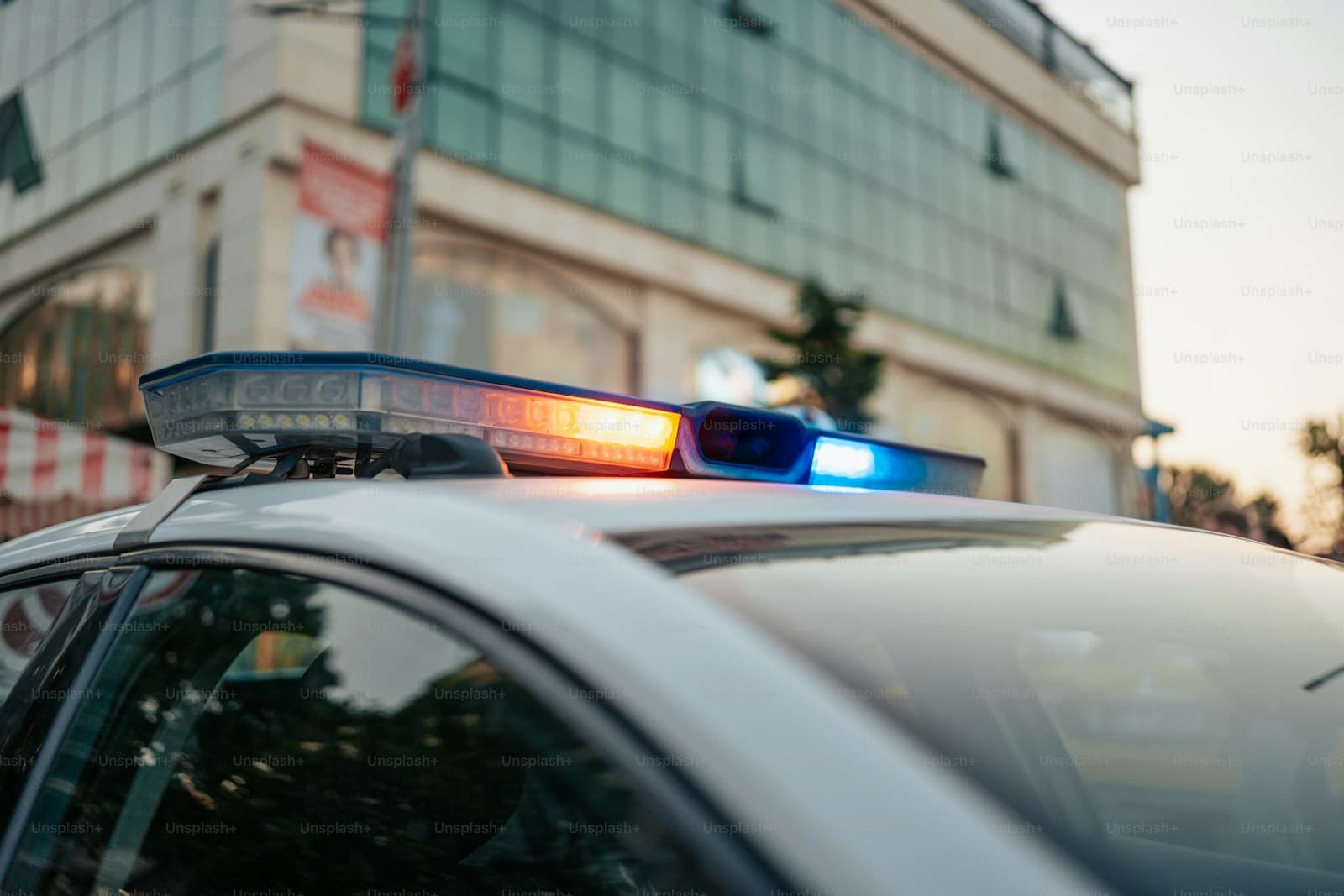 Police car with flashing red and blue emergency lights on roof, urban street background