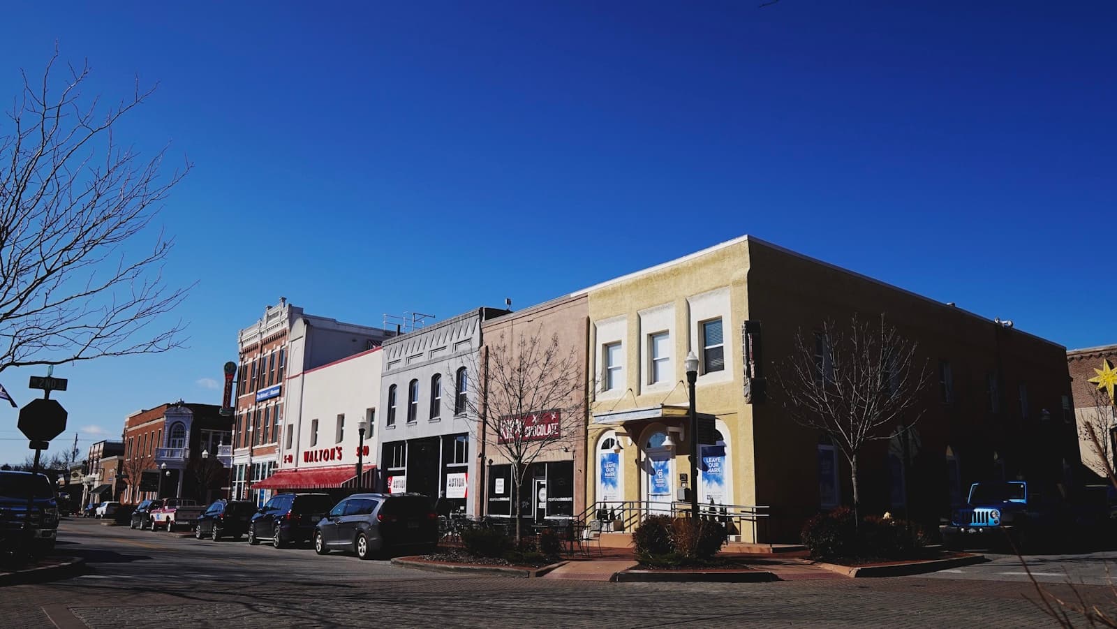 Historic downtown main street with brick buildings, storefronts, and parked cars under clear blue sky
