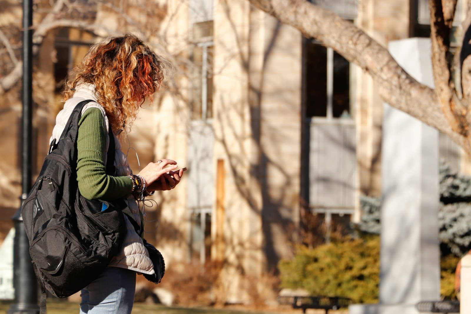 Young woman with a backpack checking her phone on a ledge among bare winter trees