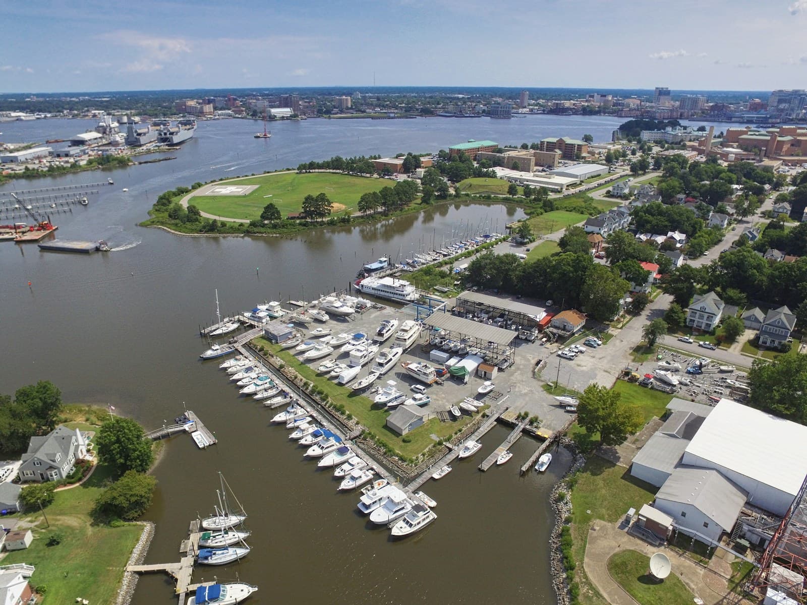 Aerial view of marina with docked boats, waterfront park, and coastal city skyline in background